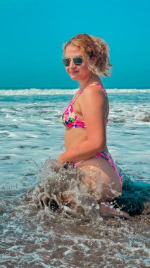 Bikinili güzel bir kadın denizde bir dalgada oturuyor..