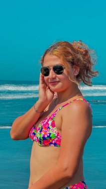 Güneşli bir günde, plajda pembe bikinili ve güneş gözlüklü güzel bir kadın. portre.