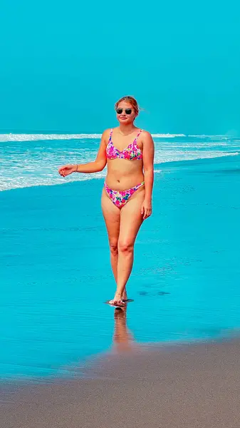 Kumsalda turkuaz suyla bikinili seksi genç kadın.