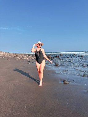 Mayolu ve şapkalı güzel bir kadın El Salvador sahilinde yürüyor.