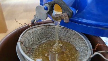 Altın bal, mevsimsel hasat sırasında doğrudan bir bal sökücüden plastik kaplara akar ve doğal üretimin zengin dokusunu gösterir..