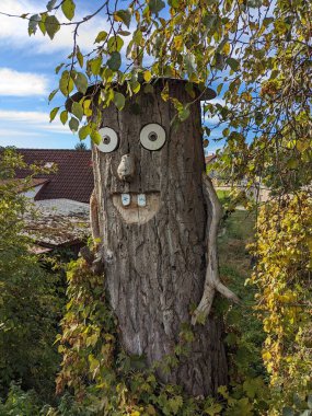 Bir ağaç gövdesinden oyulmuş komik görünüşlü iki tahta figür, bir şapkayla, halk sanatını, yaratıcılığı ve doğal bir ortamda oyuncu bir dış dekorasyonu temsil ediyor.