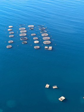 Arnavutluk 'ta gün batımında mavi, Akdeniz kıyısındaki bir balık çiftliğinin hava manzarası, Arnavutluk' un kıyı şeridi balıkçılık sanayii işletmesinin panorama manzarası -su ürünleri çiftliği balıkçılığı