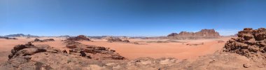 Ürdün 'deki Wadi Rum çölünün panoramik manzarası. Dağlar ve kayaların oluşturduğu düz kum üzerinde hareket eden bulutlar. Yeryüzünün güzelliğini keşfedin. Ulusal park manzarası. UNESCO