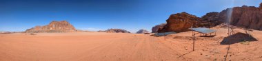 Ürdün 'deki Wadi Rum çölünün panoramik manzarası. Dağlar ve kayaların oluşturduğu düz kum üzerinde hareket eden bulutlar. Yeryüzünün güzelliğini keşfedin. Ulusal park manzarası. UNESCO