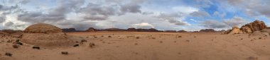 Ürdün 'deki Wadi Rum çölünün panoramik manzarası. Dağlar ve kayaların oluşturduğu düz kum üzerinde hareket eden bulutlar. Yeryüzünün güzelliğini keşfedin. Ulusal park manzarası. UNESCO