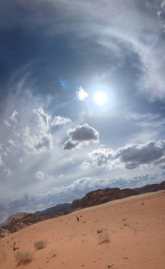 Ürdün 'deki Wadi Rum çölünün panoramik manzarası. Dağlar ve kayaların oluşturduğu düz kum üzerinde hareket eden bulutlar. Yeryüzünün güzelliğini keşfedin. Ulusal park manzarası. UNESCO