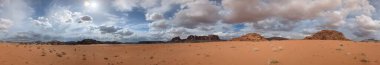 Ürdün 'deki Wadi Rum çölünün panoramik manzarası. Dağlar ve kayaların oluşturduğu düz kum üzerinde hareket eden bulutlar. Yeryüzünün güzelliğini keşfedin. Ulusal park manzarası. UNESCO