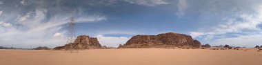 Ürdün 'deki Wadi Rum çölünün panoramik manzarası. Dağlar ve kayaların oluşturduğu düz kum üzerinde hareket eden bulutlar. Yeryüzünün güzelliğini keşfedin. Ulusal park manzarası. UNESCO