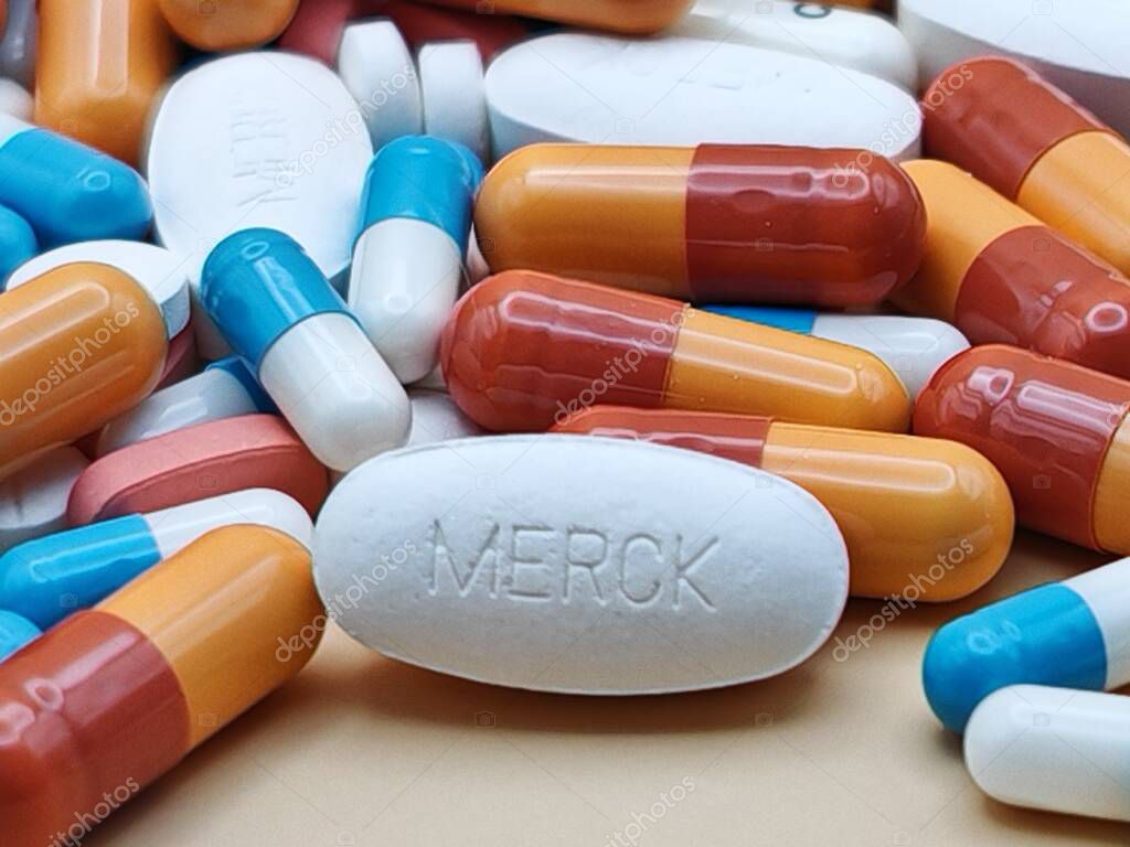 White pill with MERCK imprint placed on pile of tablets and colorful capsules in pharmaceutical visual.