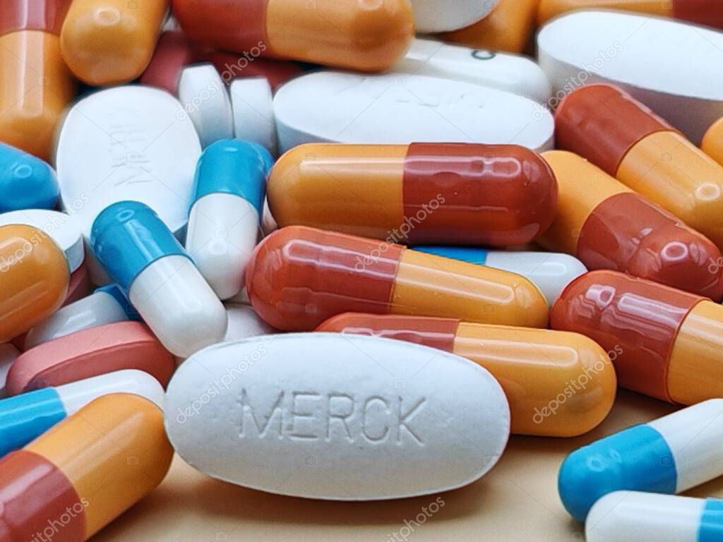 White pill with MERCK imprint placed on pile of tablets and colorful capsules in pharmaceutical visual.