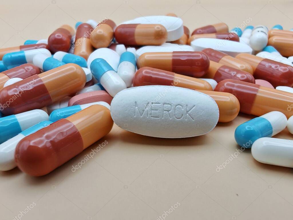 White pill with MERCK imprint placed on pile of tablets and colorful capsules in pharmaceutical visual.