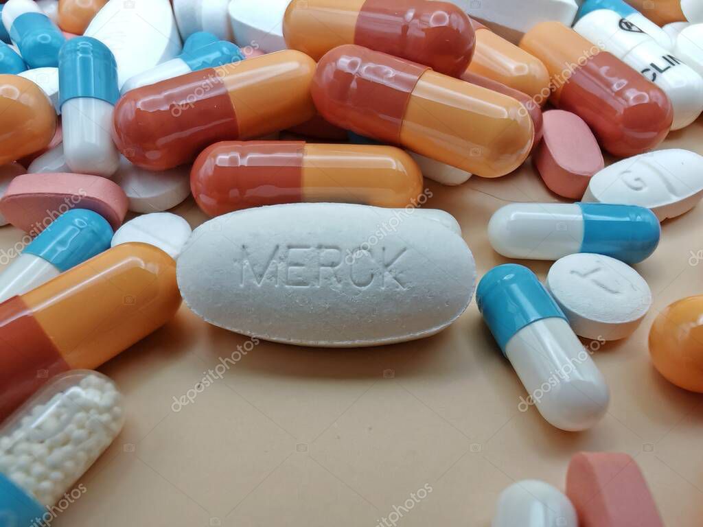 White pill with MERCK imprint placed on pile of tablets and colorful capsules in pharmaceutical visual.