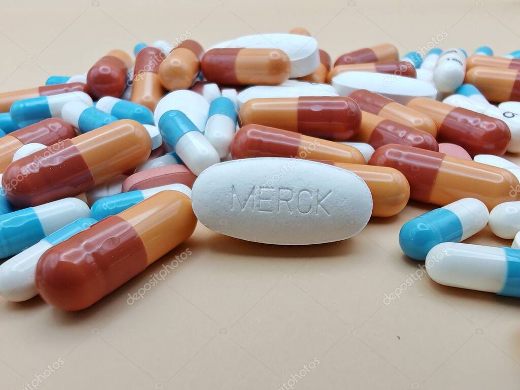White pill with MERCK imprint placed on pile of tablets and colorful capsules in pharmaceutical visual.