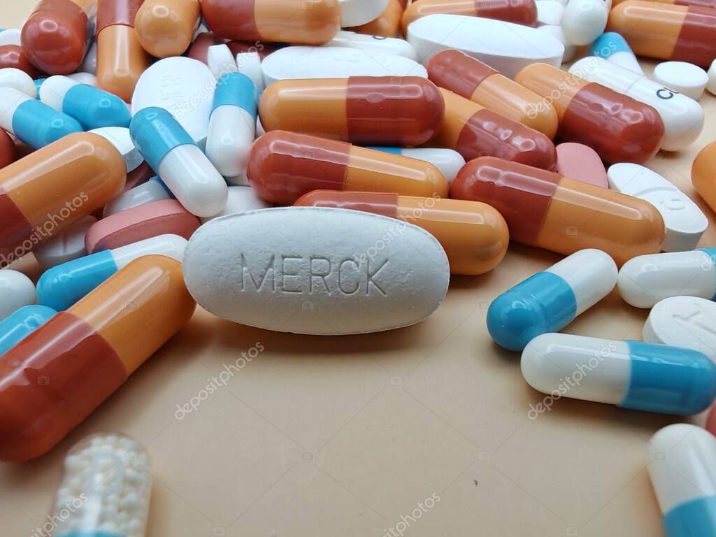 White pill with MERCK imprint placed on pile of tablets and colorful capsules in pharmaceutical visual.