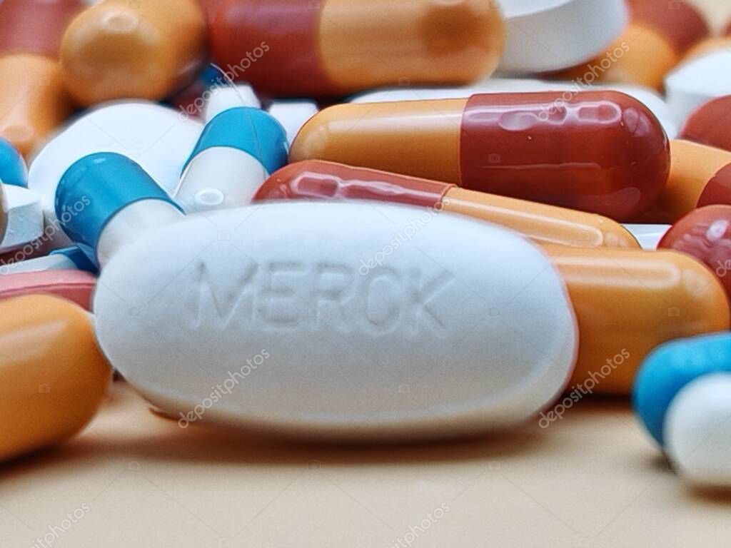 White pill with MERCK imprint placed on pile of tablets and colorful capsules in pharmaceutical visual.