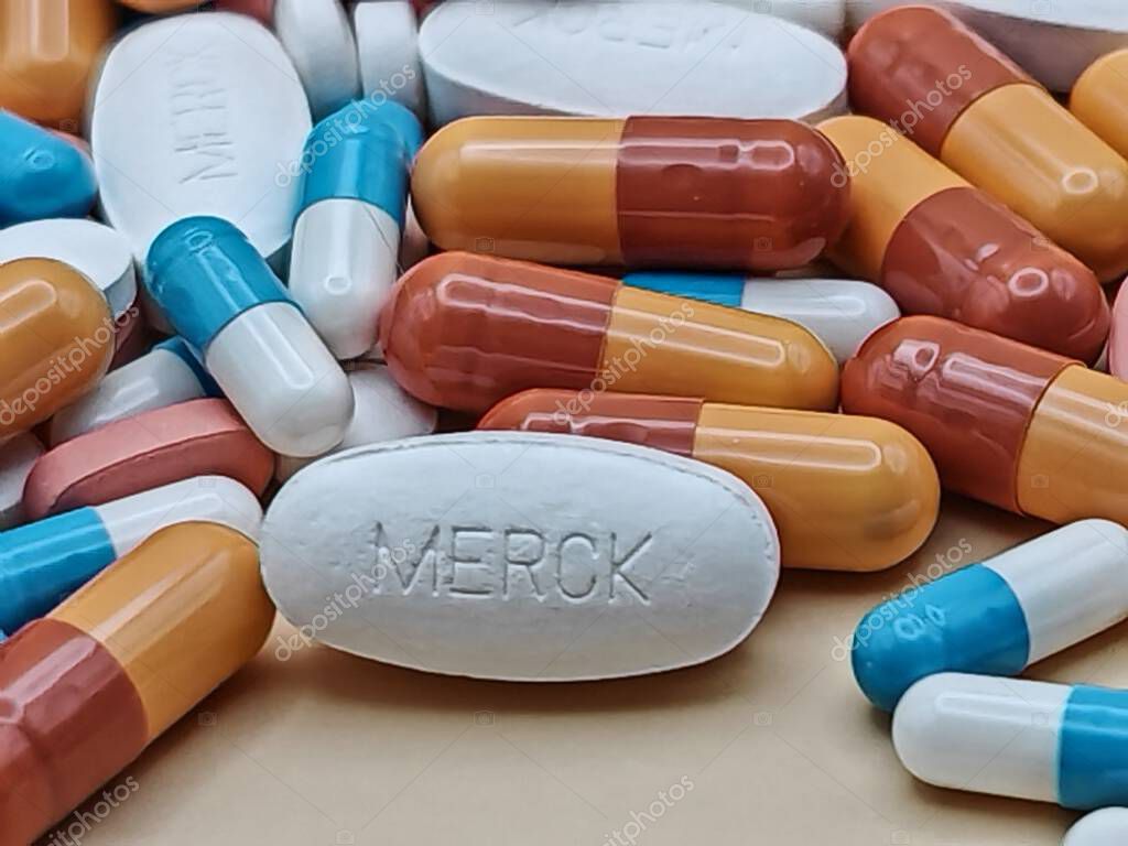 White pill with MERCK imprint placed on pile of tablets and colorful capsules in pharmaceutical visual.