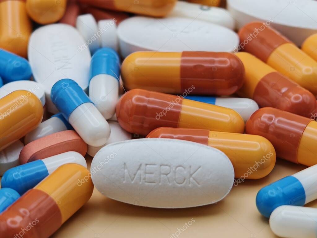 White pill with MERCK imprint placed on pile of tablets and colorful capsules in pharmaceutical visual.
