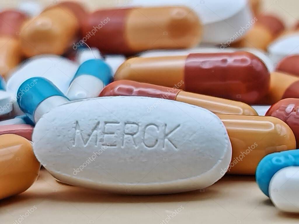 White pill with MERCK imprint placed on pile of tablets and colorful capsules in pharmaceutical visual.