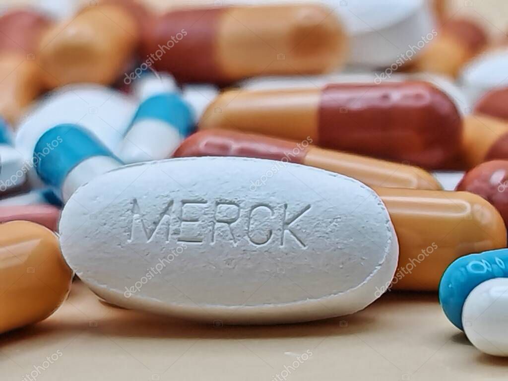 White pill with MERCK imprint placed on pile of tablets and colorful capsules in pharmaceutical visual.