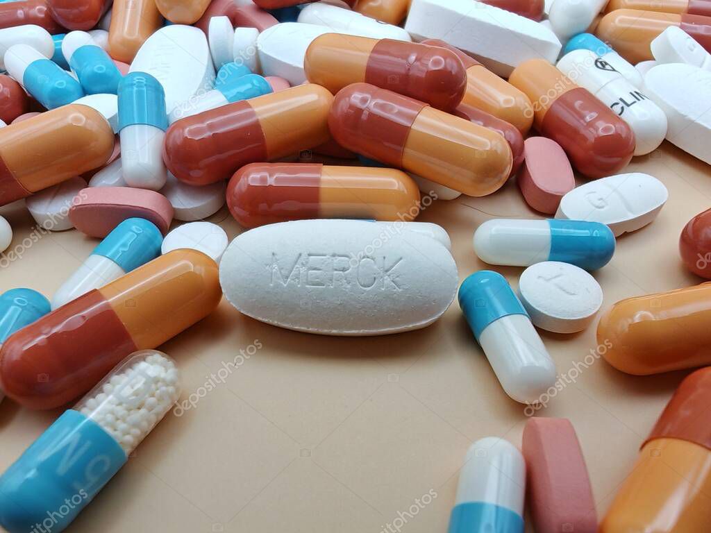 White pill with MERCK imprint placed on pile of tablets and colorful capsules in pharmaceutical visual.