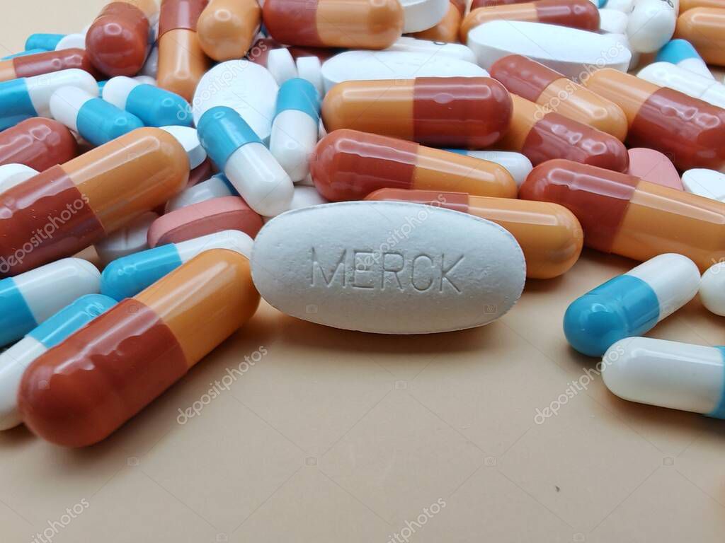 White pill with MERCK imprint placed on pile of tablets and colorful capsules in pharmaceutical visual.