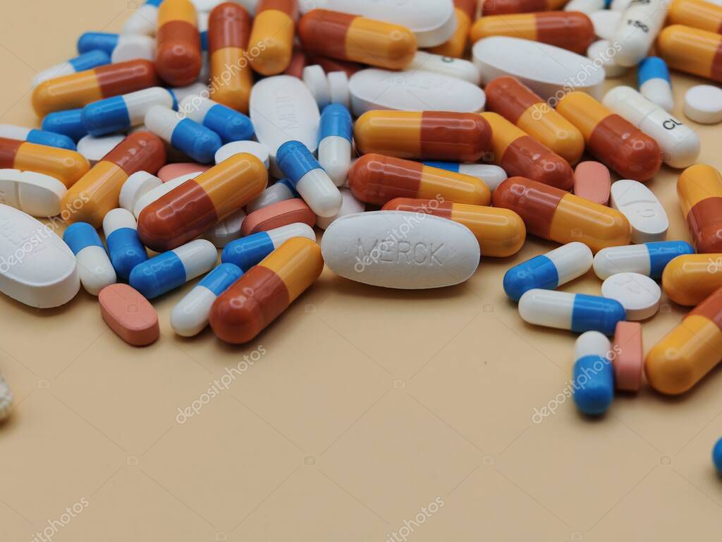 White pill with MERCK imprint placed on pile of tablets and colorful capsules in pharmaceutical visual.