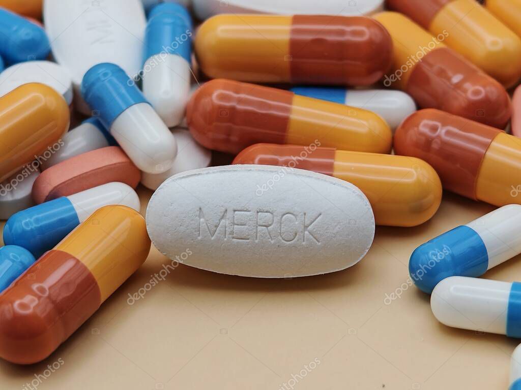 White pill with MERCK imprint placed on pile of tablets and colorful capsules in pharmaceutical visual.