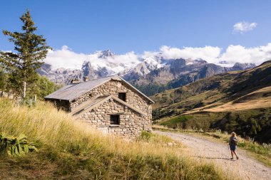 Ecrins Ulusal Parkı 'nda yürüyüş yapan, kar manzaralı Alp Dağları' nda yol boyunca antik taş evler olan bir kadın..