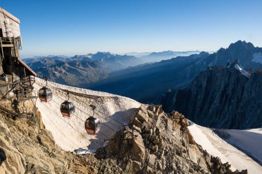 CHAMONIX, FRANCE - CUGust 2023: Fransa 'nın Chamonix kentindeki Mont Blanc zirvesine yakın güneşli bir sabahta kayalık Alpler' in üzerinden geçen kablo araba gondolları