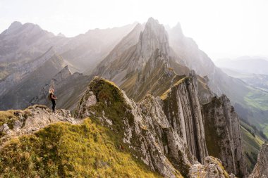 İsviçre 'de Appenzell Innerrhoden kantonunda yürüyüş yapan genç bir kadın. Arka planda kayalık dağ zirveleri.