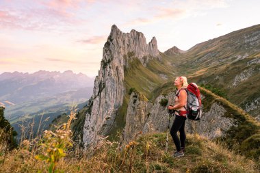 İsviçre 'de Appenzell Innerrhoden kantonunda sırt çantasıyla yürüyüş yapan genç bir kadın. Arka planda kayalık dağ zirveleri.