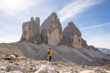 Dolomite Alpleri 'nde Tre Cime di Lavaredo Dağı yakınlarında yürüyüş yapan sarı yağmurluklu kadın. Sonbahar günü ve tepelerin üstündeki açık gökyüzü.