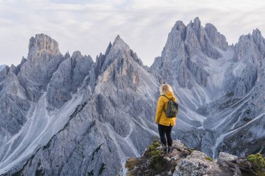Dolomite Alpleri 'nde Tre Cime di Lavaredo Dağı yakınlarında yürüyüş yapan sarı yağmurluklu kadın. Sonbahar günü ve tepelerin üstündeki açık gökyüzü.