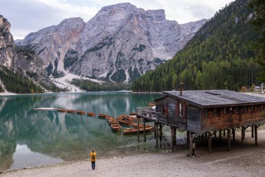 Sarı yağmurluklu kadın Braies Gölü manzarasının tadını çıkarıyor Güney Tyrol, İtalya 'daki Prag Dolomitleri.