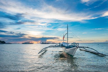 Geleneksel Banca teknesi Malapascua, Filipinler 'de çarpıcı bir günbatımına karşı demirlemiş. Dinginlik ve tropikal güzellik akşam parıltısında yakalanır..