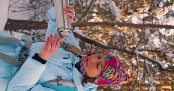 冬の雪の森をハイキングしながら 魔法瓶から暖かいお茶を飲む女性の垂直ビデオ スローモーション4K映像 — ストック動画