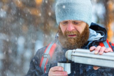 Karlı bir ormanda yürüyüş yaparken termostan sıcak çay dolduran orta yaşlı bir adam. Yakın plan fotoğraf..