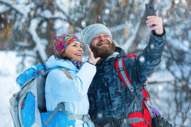 Kış yürüyüşü - internetteki video görüşmeleri sırasında karla kaplı bir ormanda orta yaşlı çift.