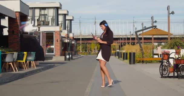 Kulaklıkla Müzik Dinleyen Mutlu Genç Bir Kadın Ofisin Dışında Yürürken — Stok video