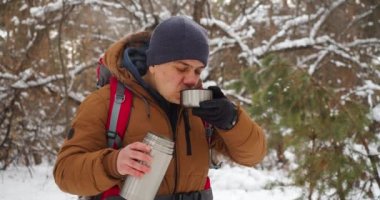 40 yaşında bir adamın kış karlı ormanlarda yürüyüş yaparken çay içtiği bir video. Yavaş çekim 4k görüntü.