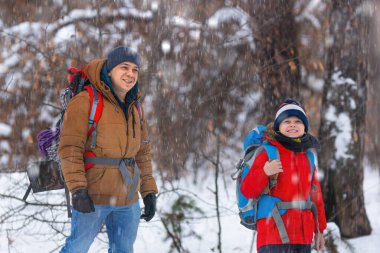 Karla kaplı bir ormanda yürüyen bir baba ve oğulun fotoğrafı. Kış yürüyüşü.