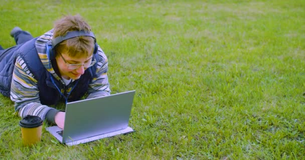 Підліток Навушниках Лежить Газоні Перед Монітором Ноутбука Він Робить Домашнє — стокове відео