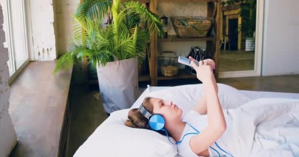 女性はスマートフォンを持ってベッドに横になっている 気まずい後ソーシャルメディアをチェックしている 現代の技術コンセプト 4K映像 — ストック動画