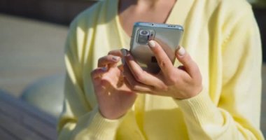 Açık havada akıllı telefonlu kadın ellerinin yakın görüntüsü. Sosyal ağlarda aktif olarak iletişim kuruyor. Yazıyor ve mesajlar gönderiyor. 4k video.