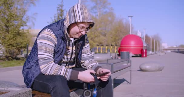 スマートフォン中毒の概念 スマートフォンやヘッドフォンを手に10代の男の子 彼は友人と屋外でチャット 4K映像 — ストック動画