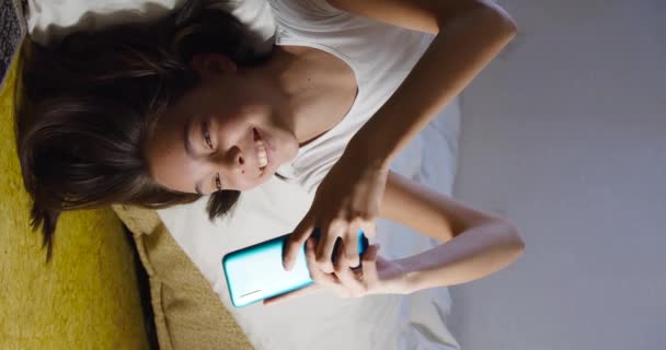 Genç Bir Kızın Fps Dikey Görüntüsü Akıllı Telefonuyla Yatakta Yatıyor — Stok video