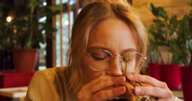 Bir kafede hamburger yiyen genç bir kadın. Yavaş çekim 4K video. Yakın çekim görünümü.