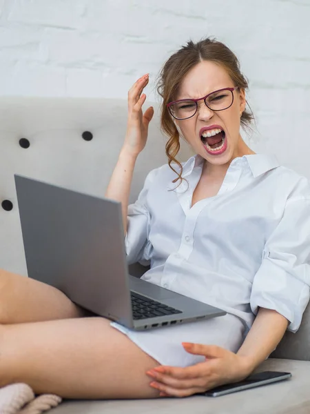 Screaming and frustrated woman in front of laptop monitor at home. Fatal error. Focus on the womans face.
