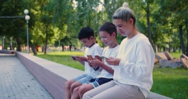 Akıllı telefon bağımlılığı. Asyalı bir aile. Anne ve iki oğlu açık havada akıllı telefonların içinde gömülü. 4k görüntü.